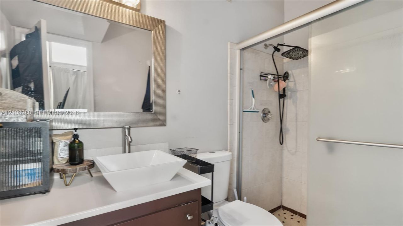 Bathroom featuring a dark wood-finish vanity, white rectangular vessel sink, framed mirror, and a walk-in shower with a glass sliding door and overhead rain shower fixture