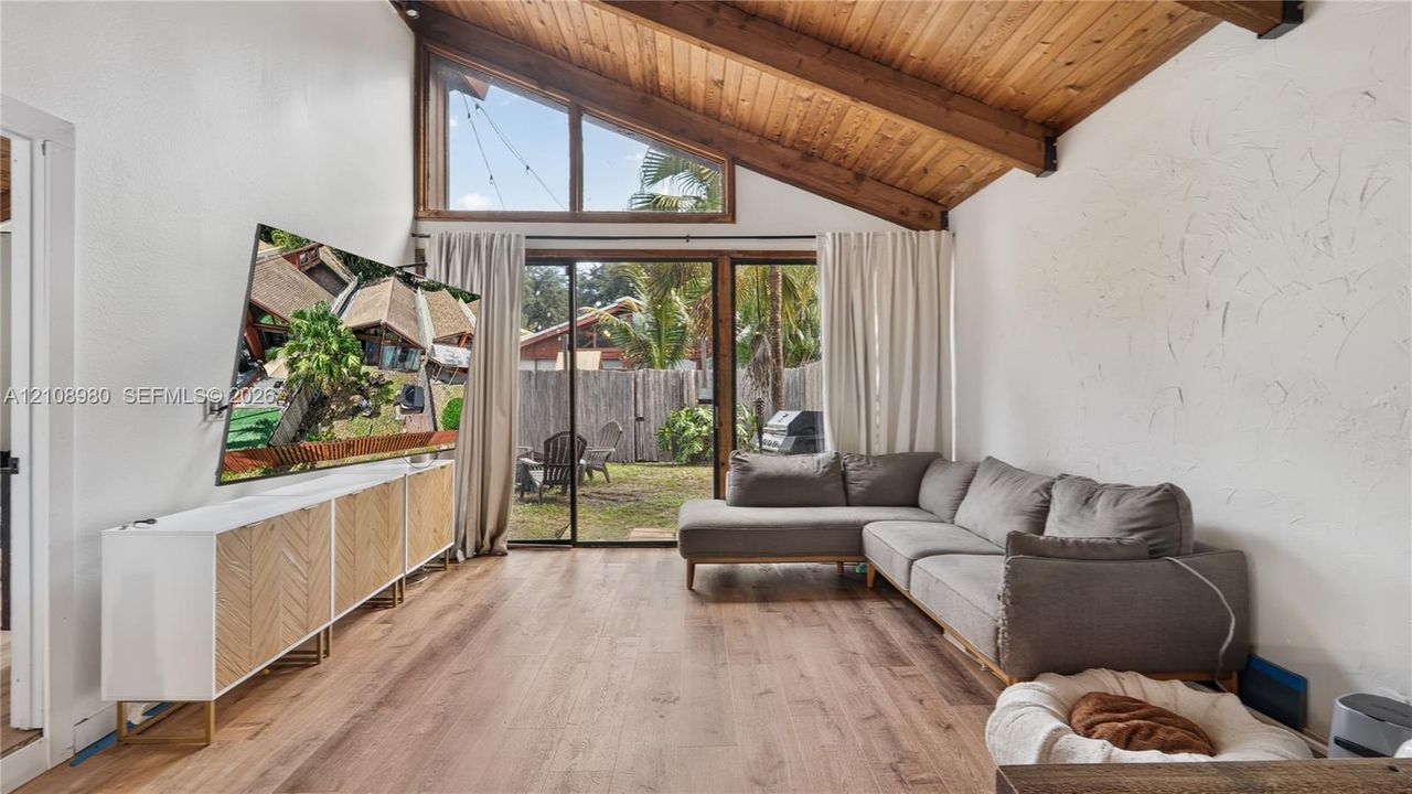Vaulted wood-plank ceiling with exposed beams, wood-finish flooring, and large sliding glass doors featuring clerestory windows
