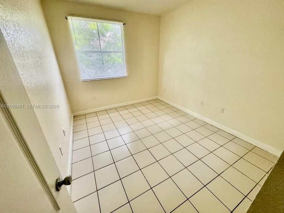 Neutral-toned room featuring ceramic tile flooring, solid-color wall finishes, and a single-pane window