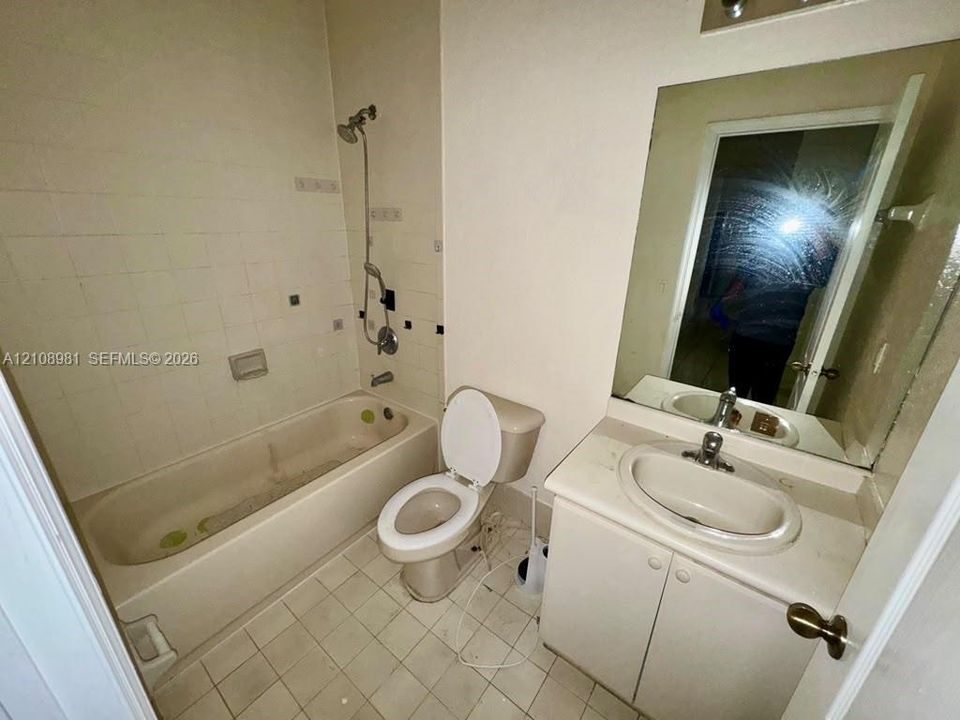 Bathroom featuring a vanity with integrated sink, large wall-mounted mirror, tub-shower combination with ceramic tile surround, and tile flooring