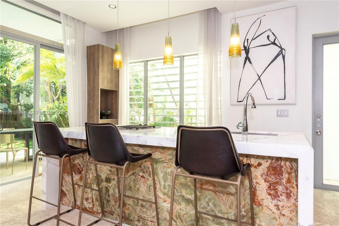 Kitchen island with a stone-finish facade, white countertop with waterfall edge, integrated cooktop, stainless steel gooseneck faucet, and three pendant light fixtures