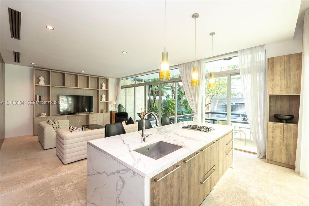 Open-concept kitchen featuring an island with a stone-finish countertop, undermount sink, and integrated stovetop, complemented by floor-to-ceiling wood-finish built-in shelving and glass sliding doors