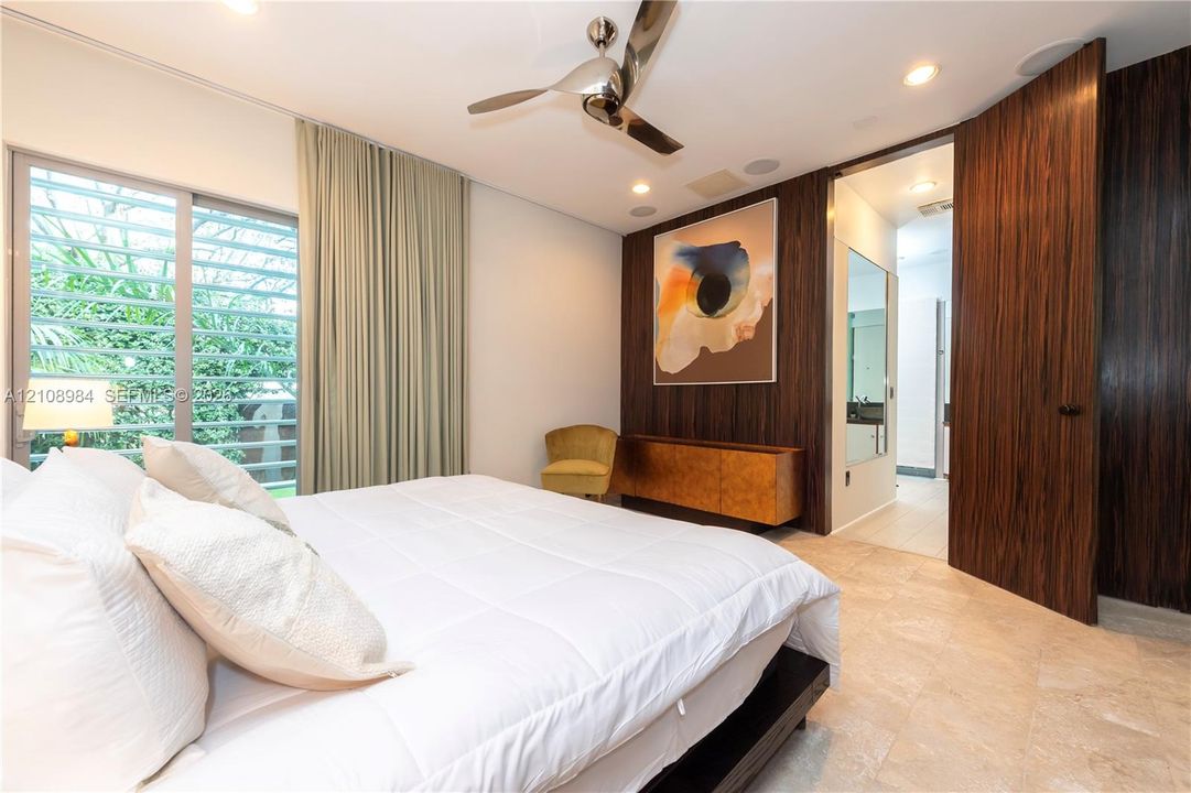 Room featuring natural stone flooring, floor-to-ceiling wood-finish paneling, louvered sliding glass doors, recessed lighting, and a modern metal ceiling fan