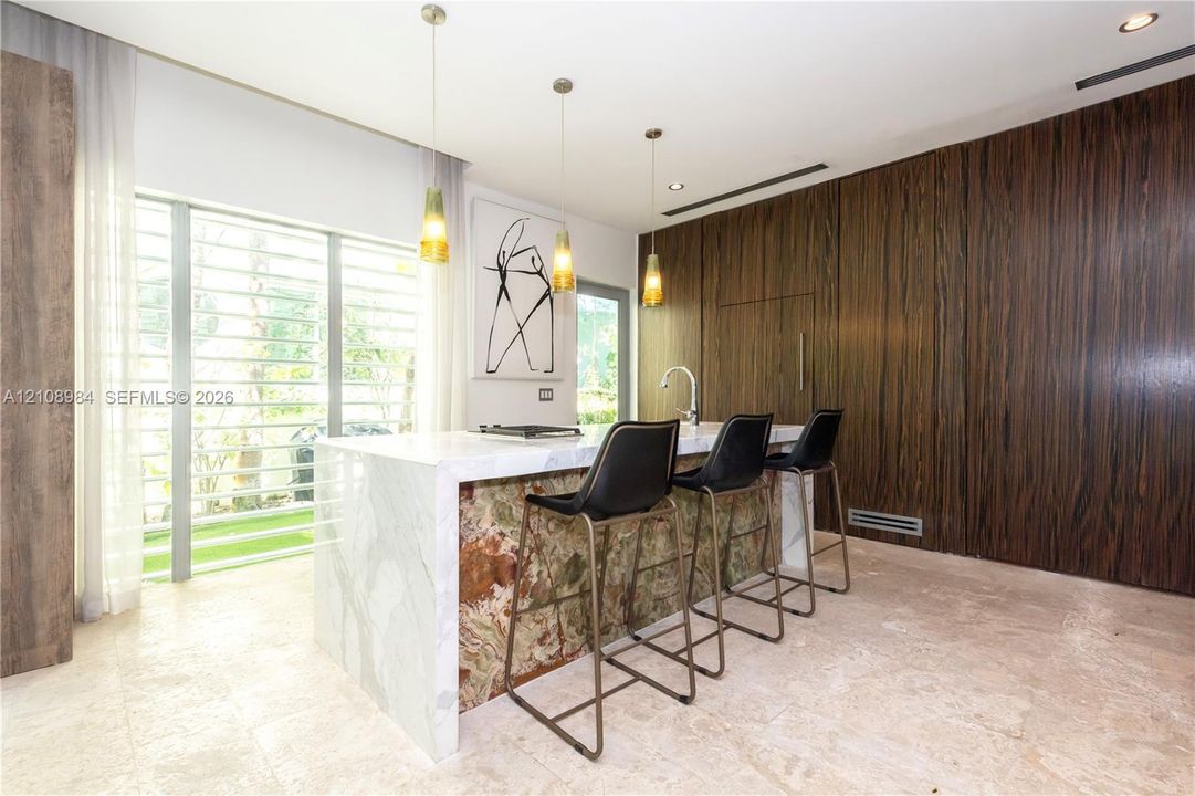 Kitchen island featuring a waterfall stone countertop with a contrasting decorative stone base, floor-to-ceiling wood-finish paneling, stone flooring, and suspended pendant lighting