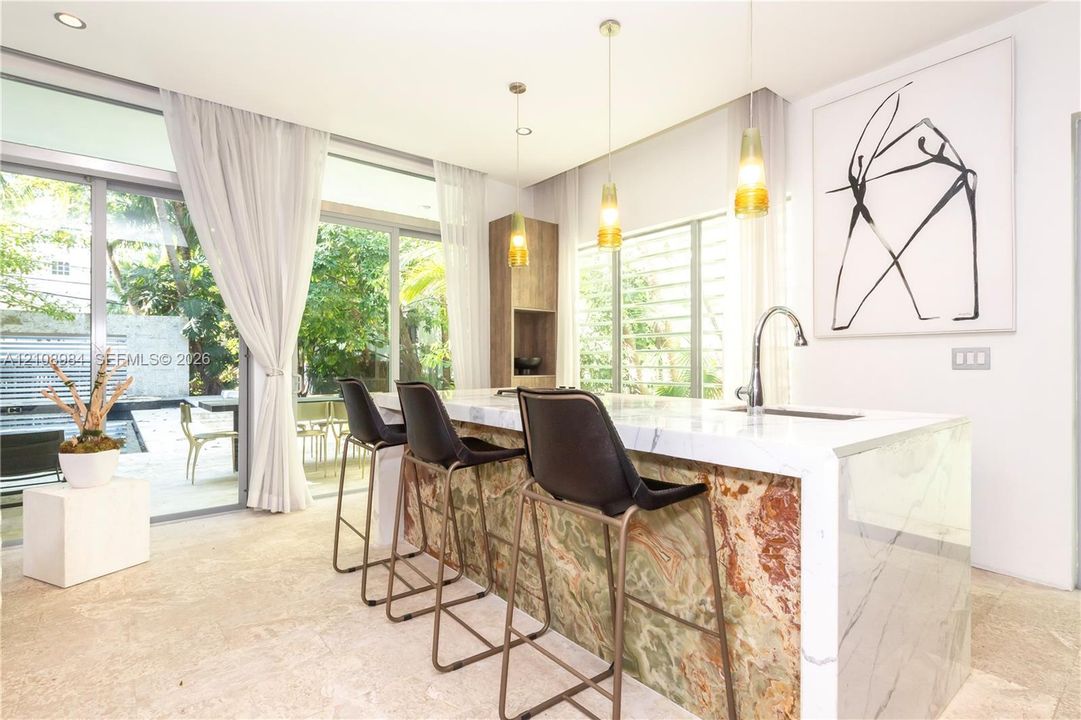 Kitchen island featuring a waterfall countertop with a stone-finish side panel and built-in cabinetry, polished stone flooring, and suspended pendant lighting