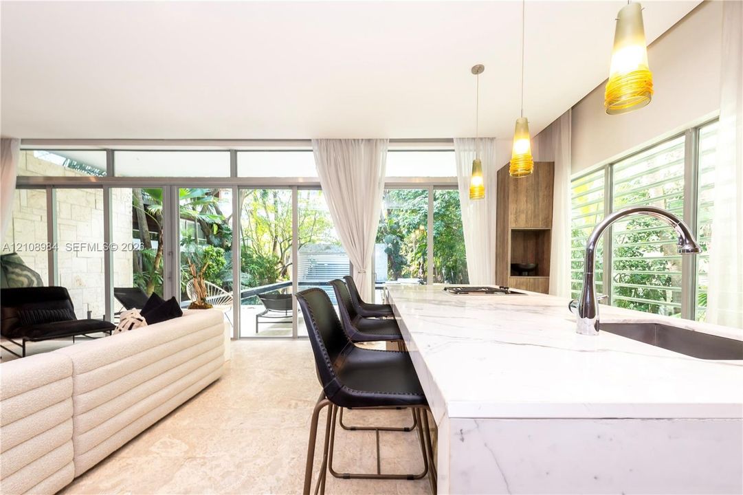 Kitchen island featuring a waterfall-edge stone countertop, undermount sink, and chrome gooseneck faucet, complemented by floor-to-ceiling glass panel walls and textured stone wall accents