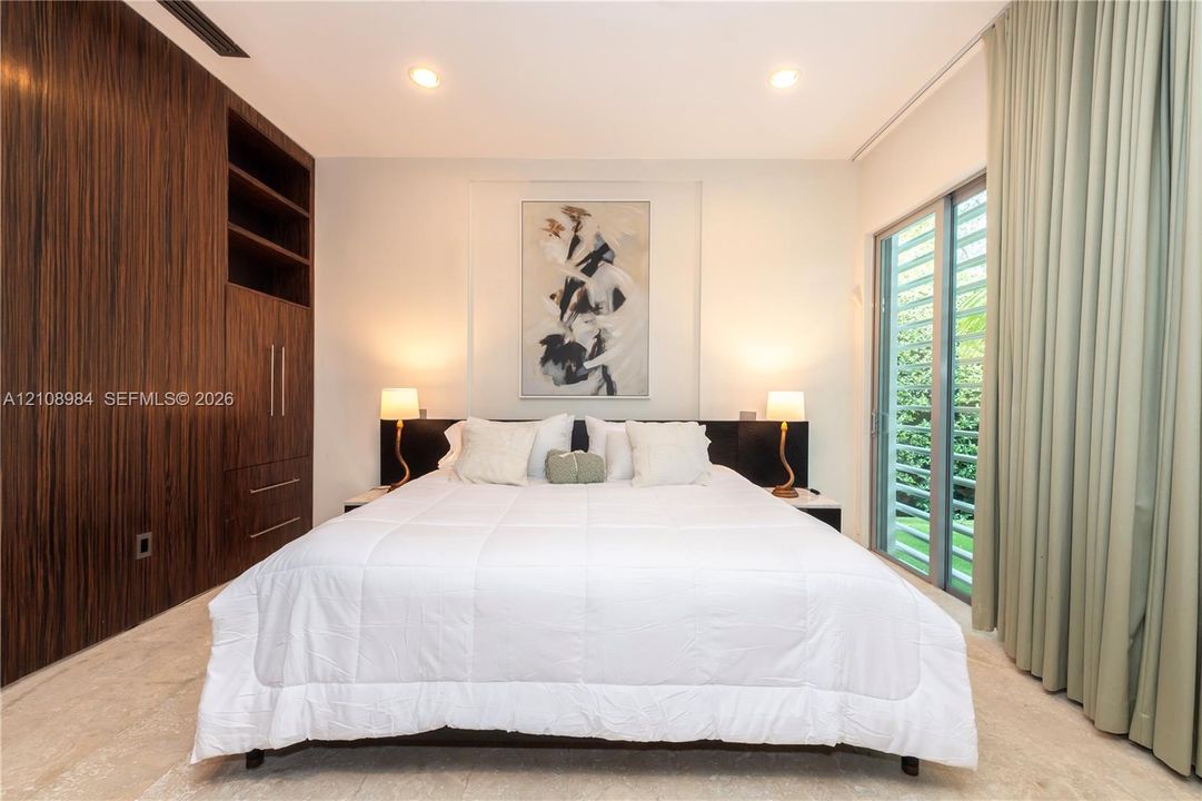 Room featuring floor-to-ceiling wood-grain cabinetry, stone flooring, recessed lighting, and sliding glass doors with louvered panels