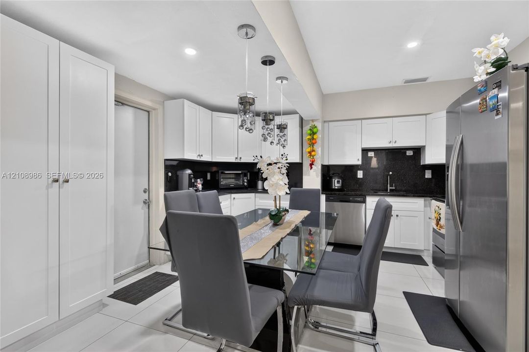 Kitchen featuring white shaker-style cabinetry, contrasting dark stone countertops, stainless steel appliances, polished tile flooring, and a trio of decorative pendant lights