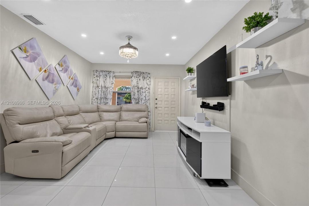 Living area featuring polished tile flooring, recessed lighting, a decorative flush-mount ceiling fixture, and wall-mounted shelving