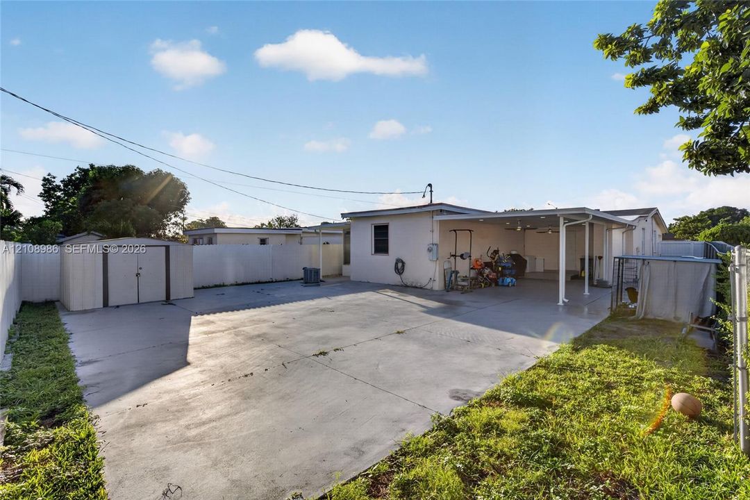 Concrete patio area featuring a covered carport, a detached metal storage shed, and perimeter fencing