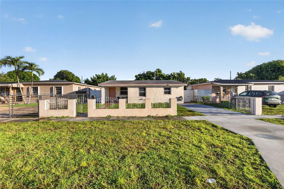 Single-story residence featuring a low-slope roof, stucco exterior, concrete driveway, and front perimeter wall with metal fencing