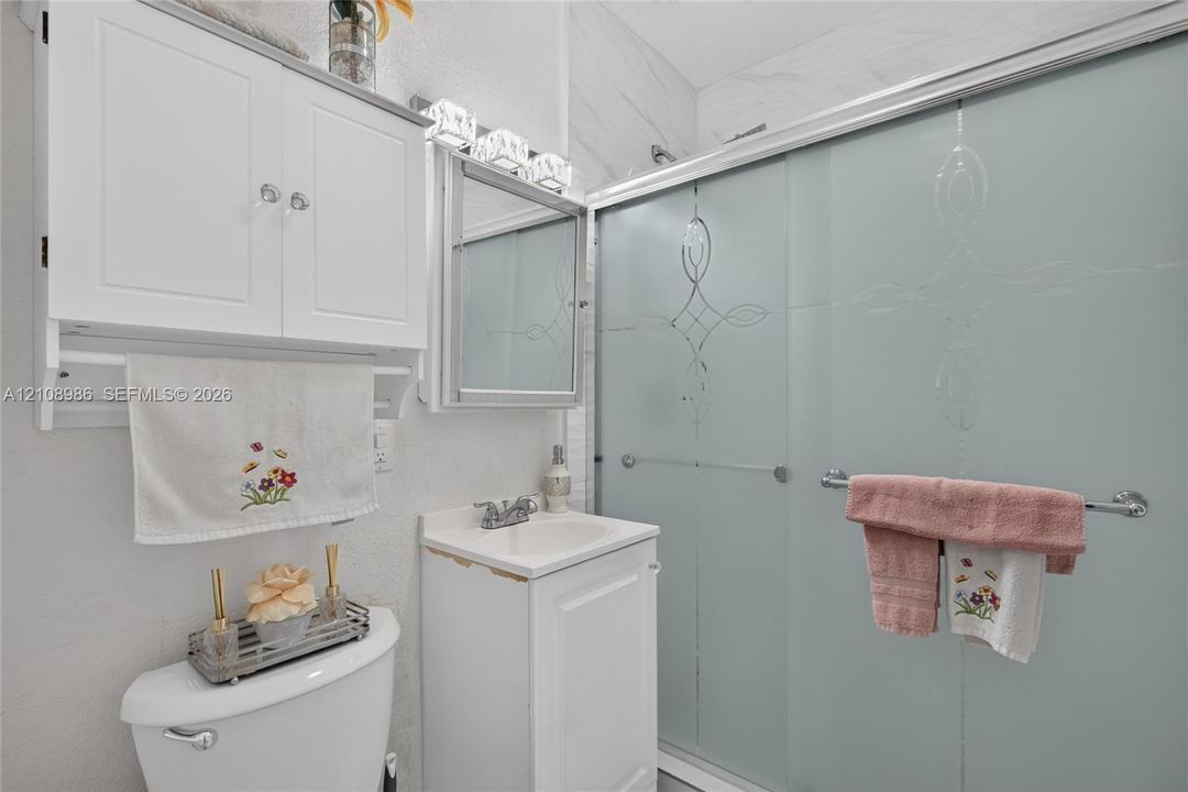 Bathroom featuring a white vanity cabinet with an integrated sink, frosted sliding glass shower doors with etched detailing, wall-mounted storage cabinetry, and a mirrored medicine cabinet