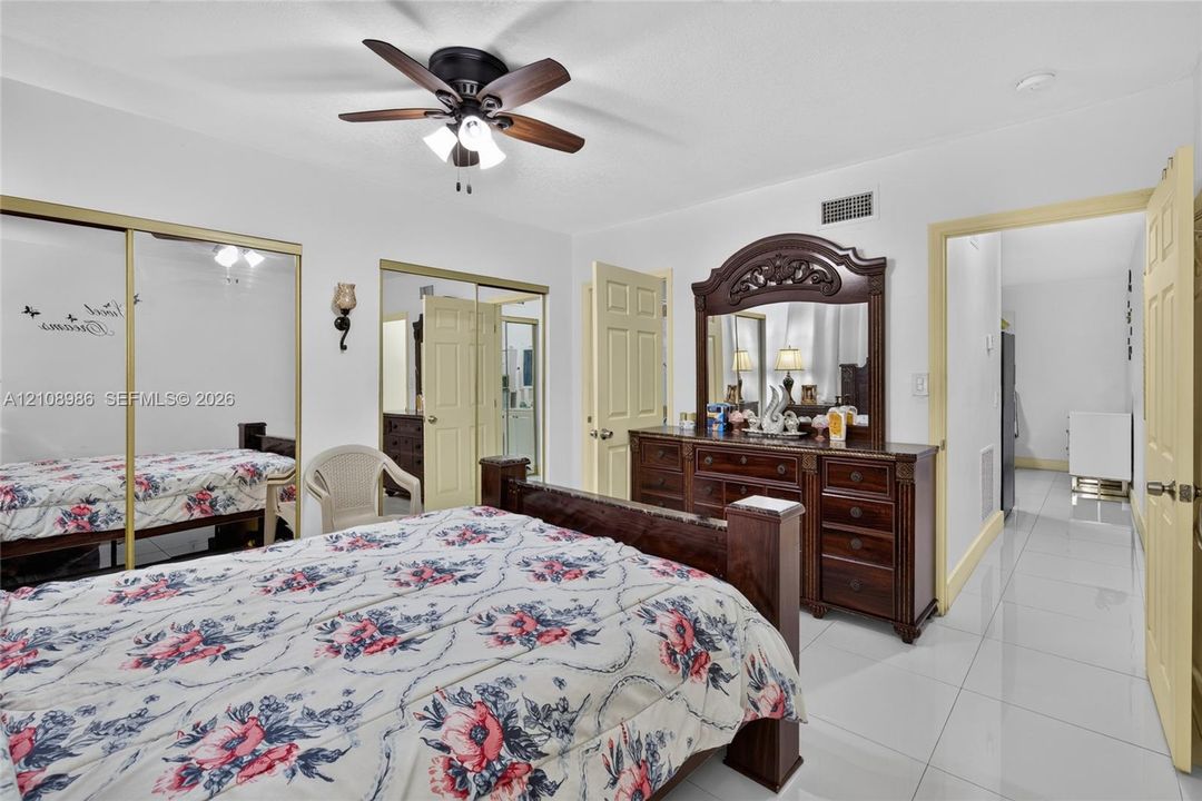 Room featuring large-format tile flooring, dual closets with floor-to-ceiling mirror sliding doors, and a central ceiling fan with integrated lighting