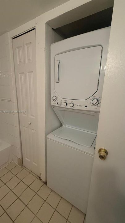 Stacked laundry unit with white appliances and bi-fold closet door on tiled flooring