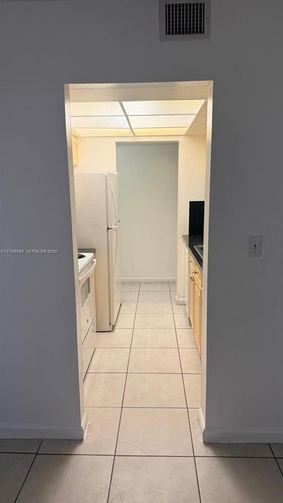 Kitchen featuring tile flooring, light wood-finish cabinetry, solid surface countertops, and an integrated drop-ceiling lighting panel