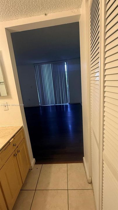 Bathroom vanity with stone-finish countertop, light-wood cabinetry, white tile flooring, and louvered closet doors