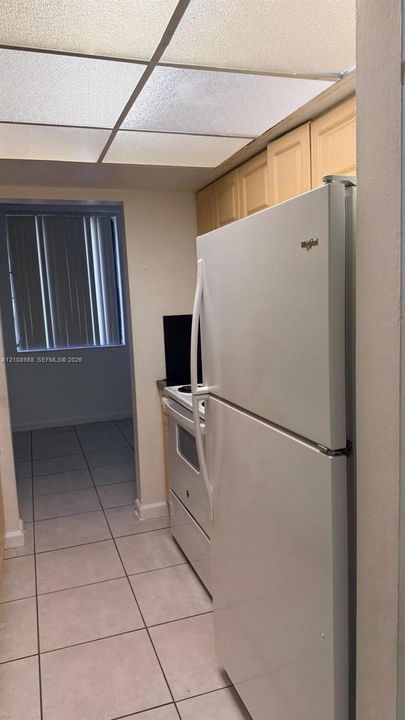 Kitchen featuring light wood cabinetry, white appliances, square tile flooring, and a drop-panel ceiling fixture