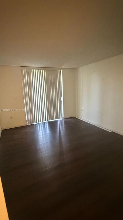 Room with wood-finish flooring, neutral-toned walls, and floor-to-ceiling sliding glass doors with vertical blinds