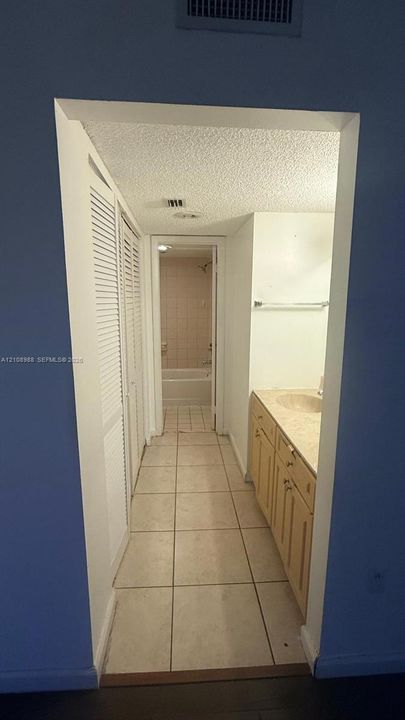 Bathroom featuring tiled flooring, a vanity with a stone-finish countertop, an integrated sink, and floor-to-ceiling louvered closet doors