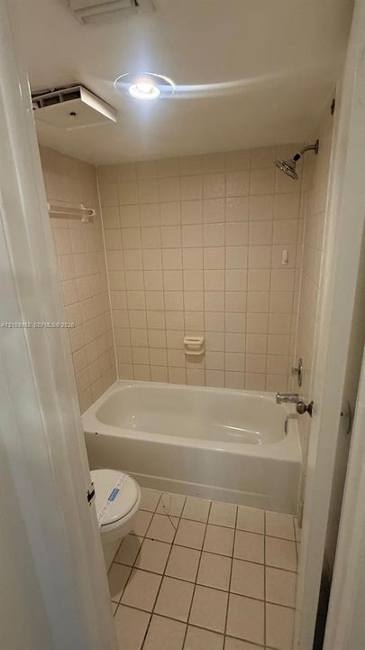 Bathroom featuring a built-in bathtub with shower head, tiled walls, ceramic floor tile, and integrated recessed lighting