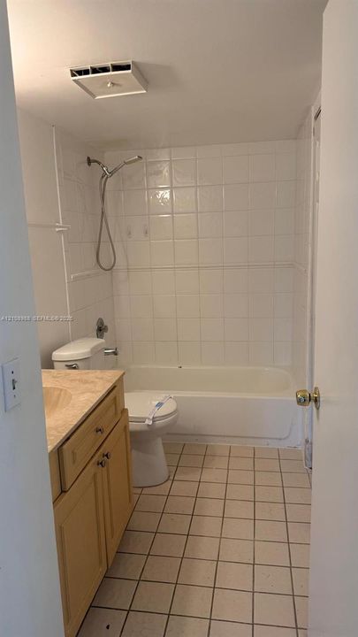 Bathroom featuring a vanity with a stone-finish countertop, white tile tub surround, handheld shower fixture, and square tile flooring