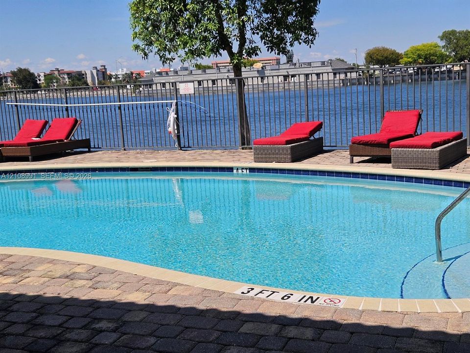 Curved in-ground swimming pool with stone paver decking and a metal safety perimeter fence