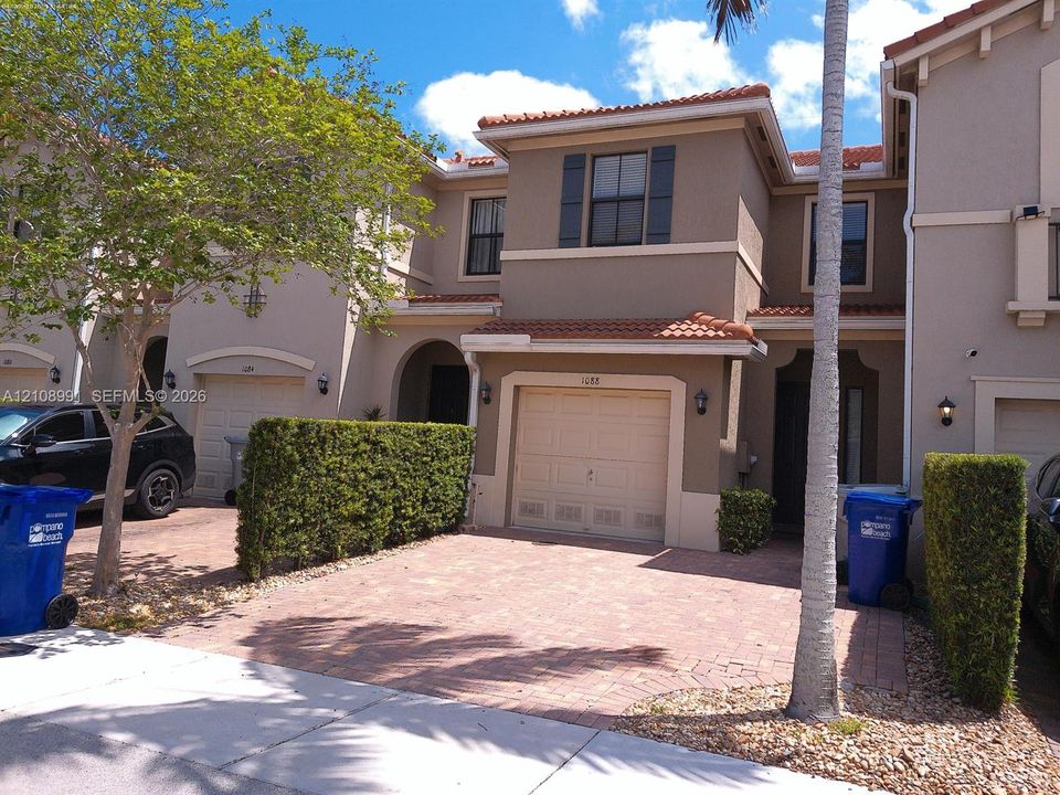 Two-story residence featuring a terracotta-tile roof, paved driveway, single-car garage, shuttered windows, and arched entryway