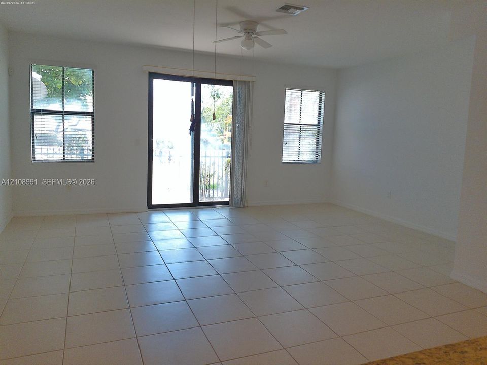 Neutral-toned tile flooring, sliding glass door with exterior access, multiple grid-patterned windows, and a ceiling-mounted fan with light fixture