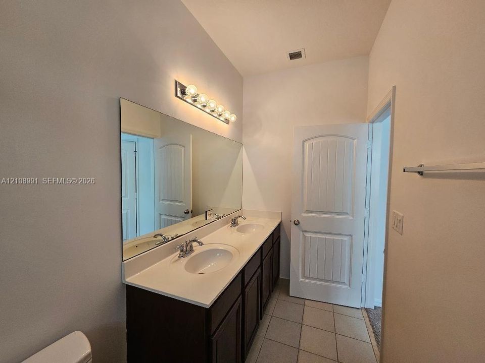 Double vanity featuring a light-toned countertop with integrated dual basins, dark-finish cabinetry, full-width wall mirror, and chrome-finish fixtures