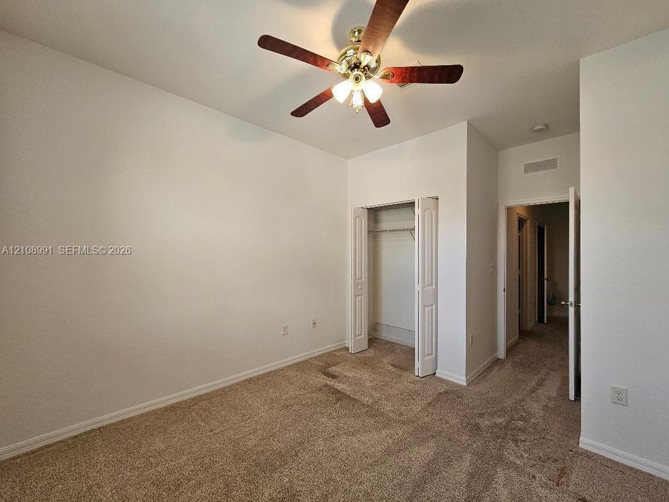 Neutral wall tones, carpeted flooring, built-in closet with folding doors, and a ceiling-mounted light fixture with a fan