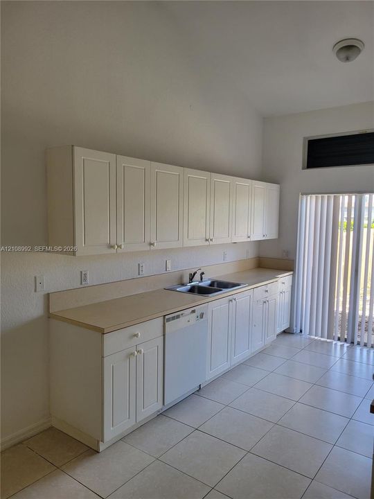 Kitchen featuring white shaker-style cabinetry, solid-surface countertops, dual-basin stainless steel sink, integrated dishwasher, and tile flooring