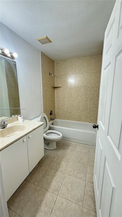 Bathroom featuring a white vanity cabinet with an integrated sink, ceramic tile flooring, a tub-shower combination with tiled surround, and wall-mounted vanity lighting