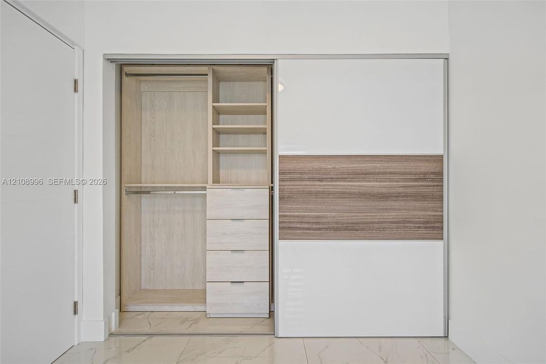 Built-in closet featuring floor-to-ceiling sliding panels, integrated wood-finish shelving, four soft-close drawers, and metal hanging rods