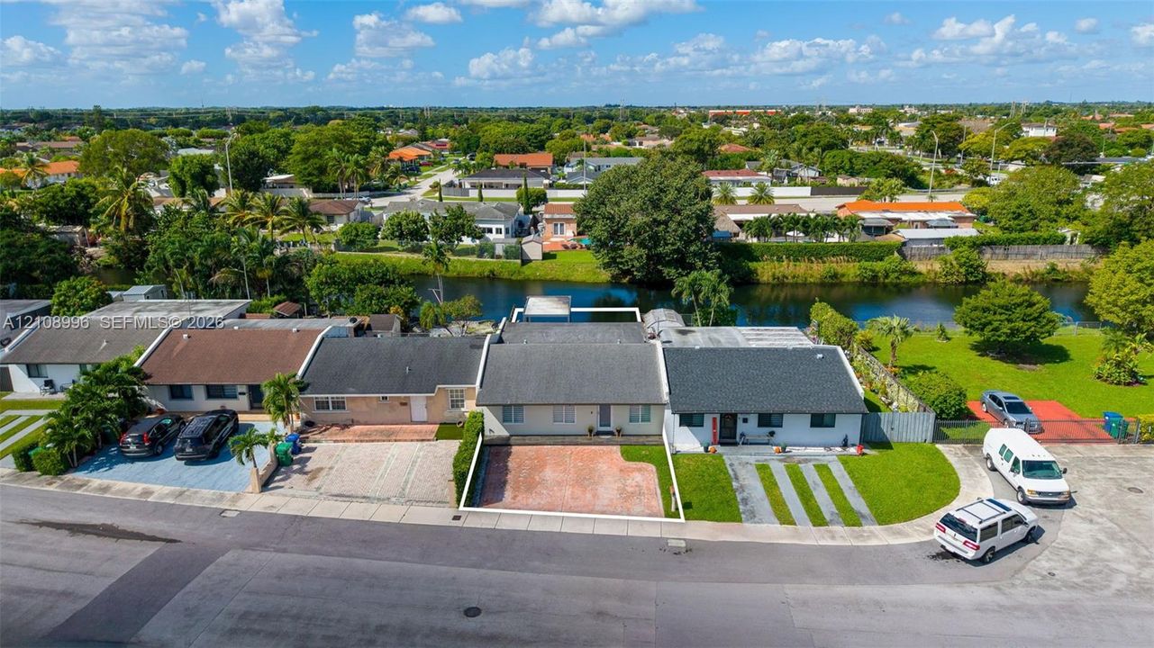 Aerial perspective of a single-story residence featuring a shingled roof, a paved front courtyard, and direct canal frontage with a manicured rear lawn