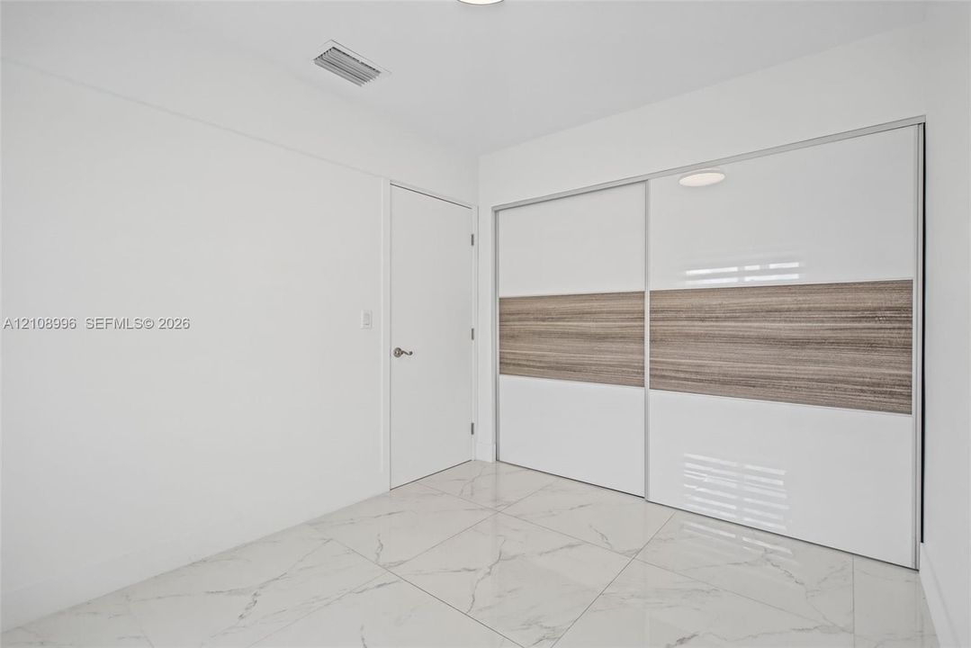 Large-format polished tile flooring featuring a veined pattern, dual sliding closet doors with high-gloss white and wood-finish detailing, and a solid-core interior door