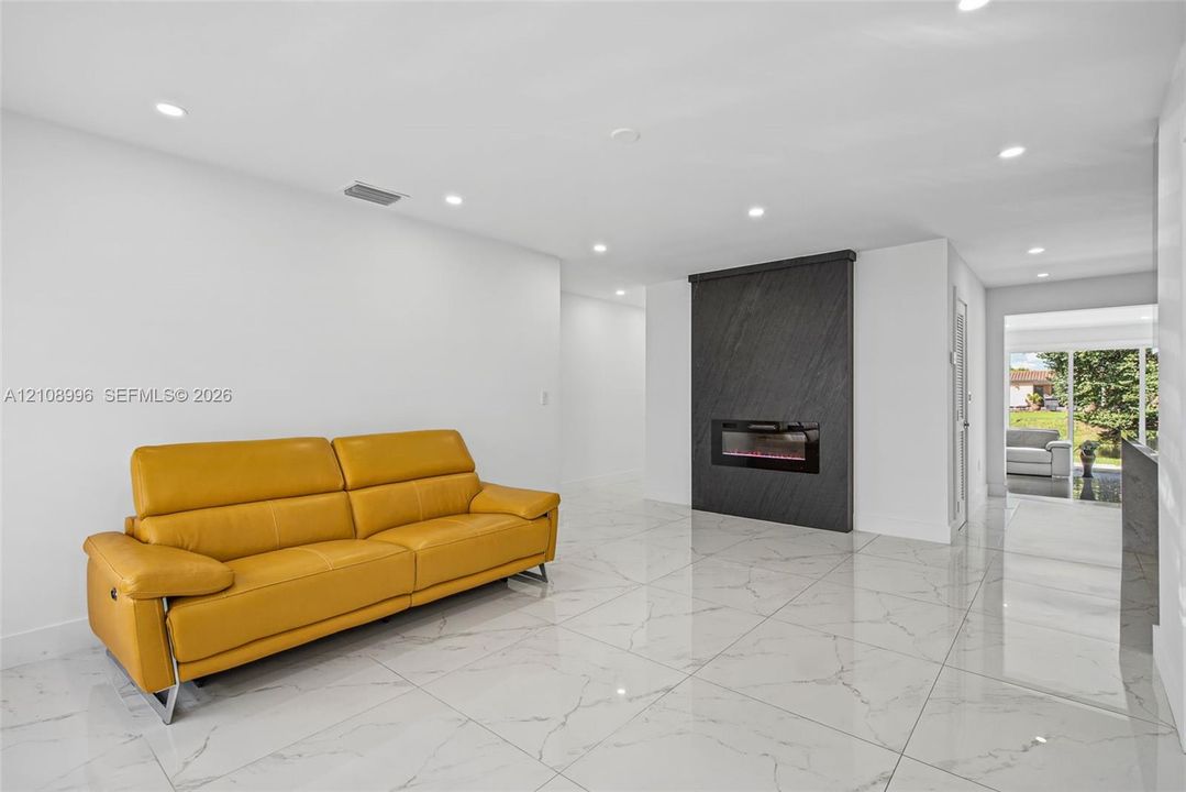 Large-format stone-style flooring, recessed lighting, and a focal wall featuring a built-in linear electric fireplace