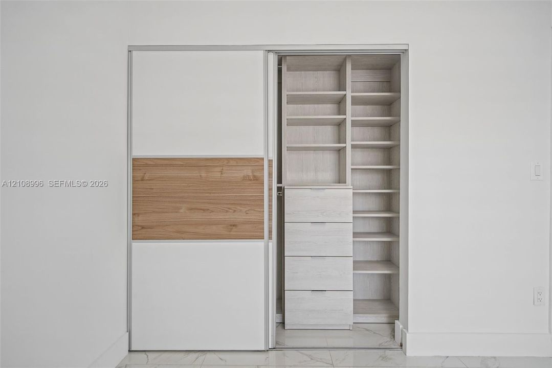 Built-in closet featuring sliding doors with wood-finish accents, custom shelving, and a four-drawer storage unit