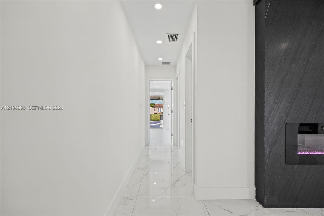 Hallway featuring large-format stone-look porcelain tile flooring, recessed ceiling lighting, and a floor-to-ceiling charcoal-toned stone fireplace surround with a built-in linear electric insert