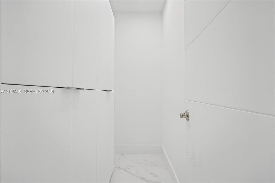 Built-in floor-to-ceiling cabinetry featuring clean-lined, white panel doors with minimalist hardware and white stone-finish tile flooring