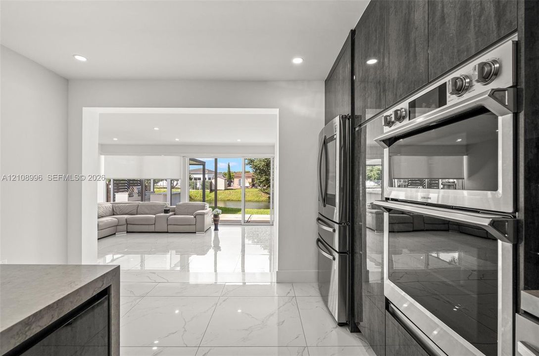 Modern kitchen featuring sleek, high-gloss charcoal cabinetry, integrated stainless steel double wall ovens, a stainless steel refrigerator, and large-format porcelain tile flooring