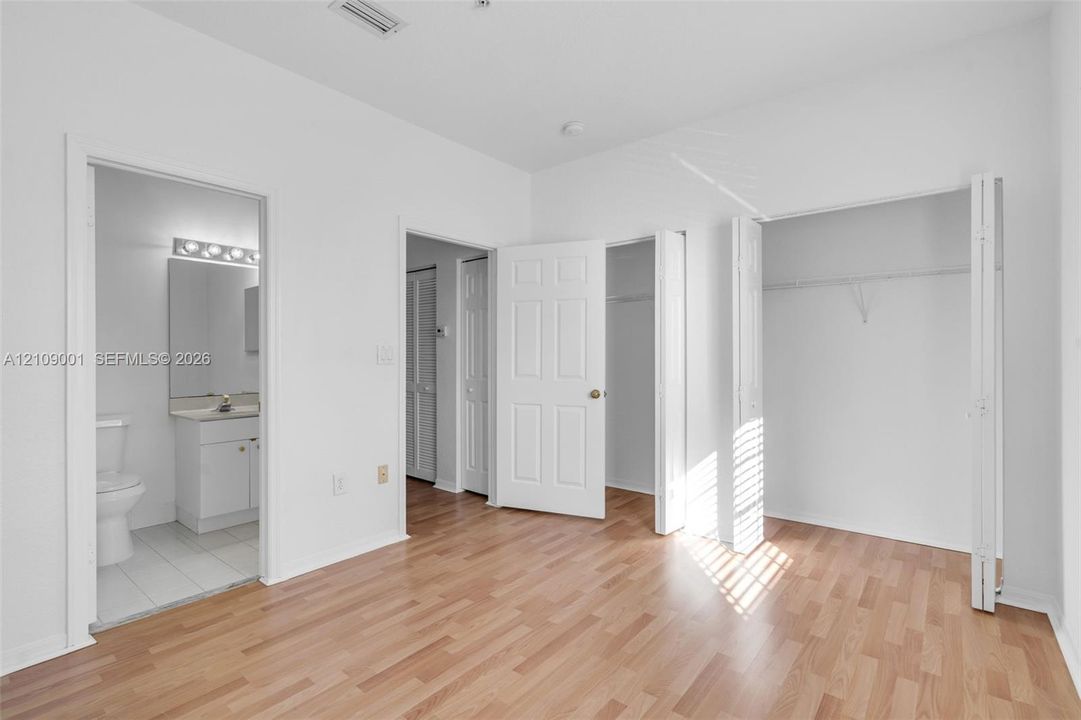Room featuring wood-finish flooring, two bi-fold closets, and an integrated bathroom with a vanity and mirror lighting