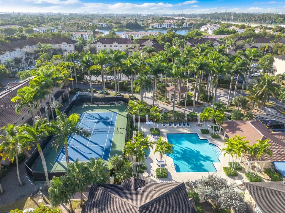 Aerial perspective featuring a hard-surface tennis court, a swimming pool, mature palm trees, and tiled-roof structures