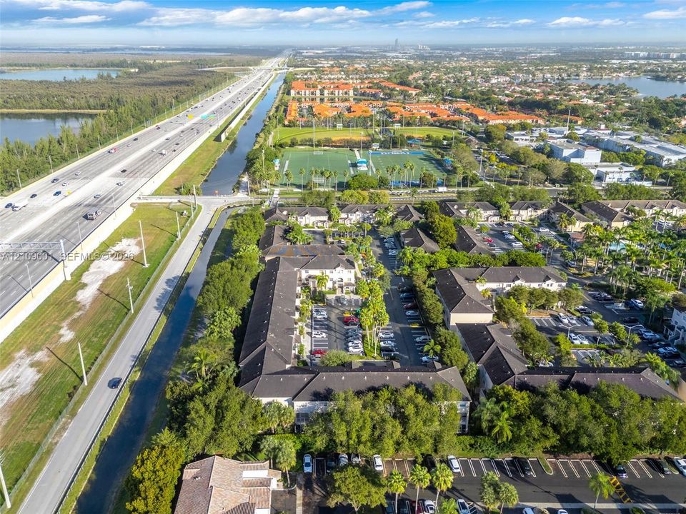 Aerial perspective of a multi-unit complex featuring shingled rooflines, exterior courtyards, paved surface parking, and extensive mature landscaping