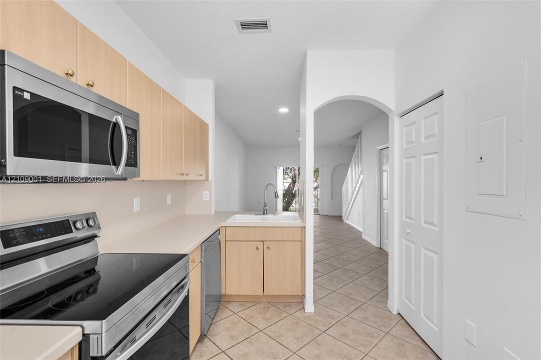 Kitchen featuring light wood cabinetry, stainless steel appliances, neutral solid-surface countertops, tile flooring, and an arched entry