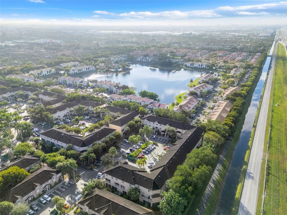 Aerial perspective of residential community featuring multi-story buildings, dark tile roofing, expansive lakefront footage, and surrounding mature landscaping