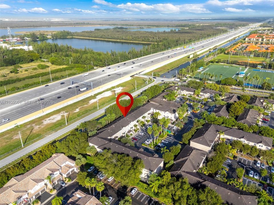 Aerial perspective of multi-family complex featuring tile roof construction, asphalt parking areas, and mature palm landscaping