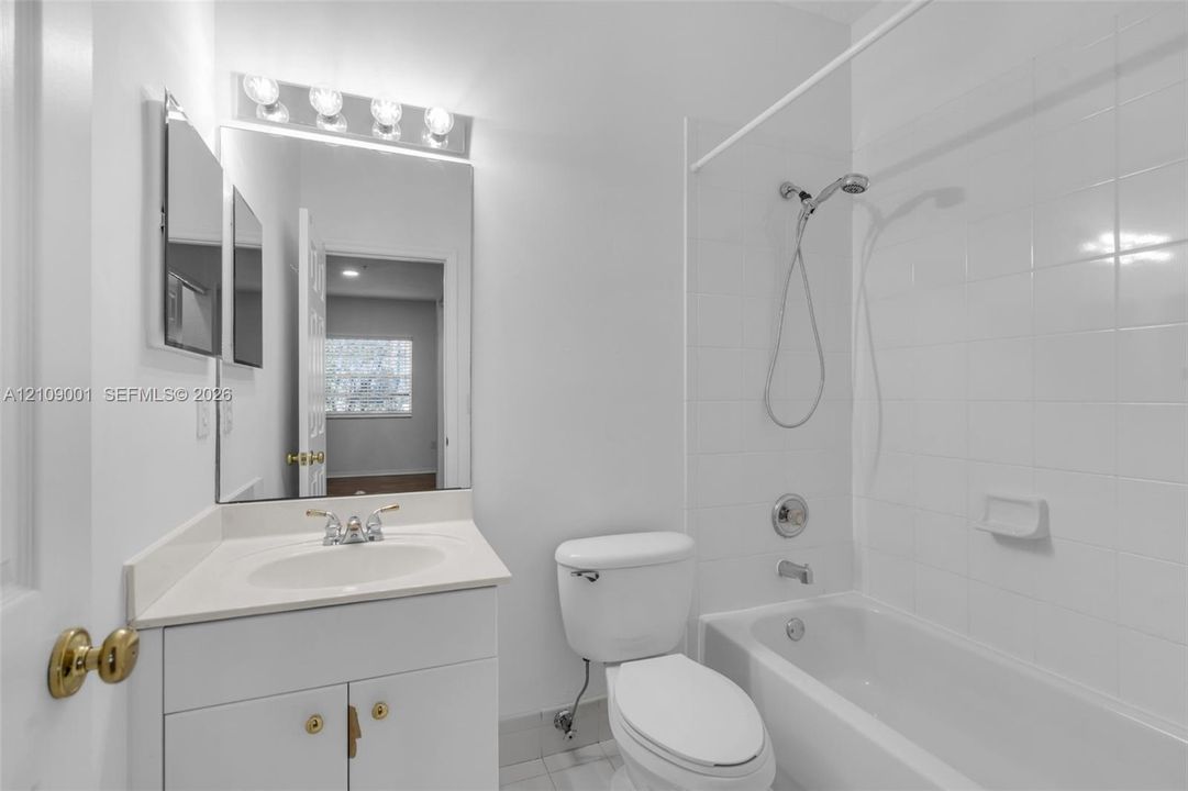 Bathroom featuring a white vanity cabinet with an integrated sink, a wall-mounted rectangular mirror, polished chrome faucet hardware, and a tub-shower combination with white wall tile