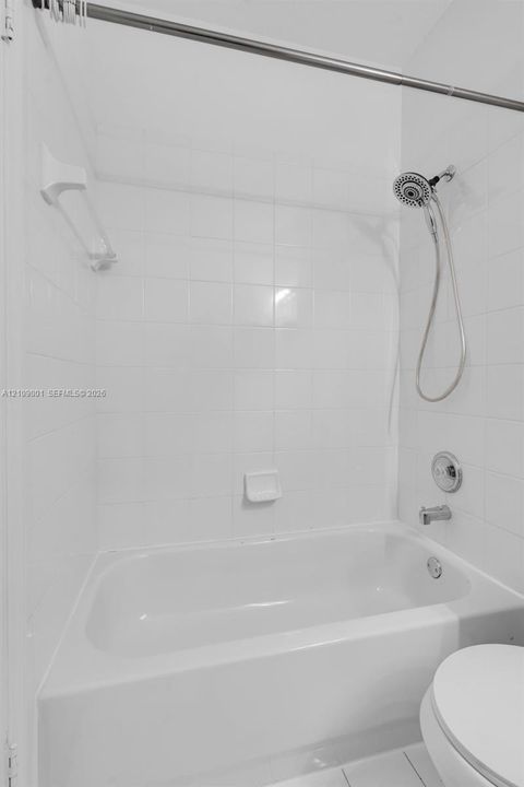 Shower and bathtub combination featuring white ceramic wall tile, a built-in soap dish, a handheld shower head, and a chrome-finish faucet