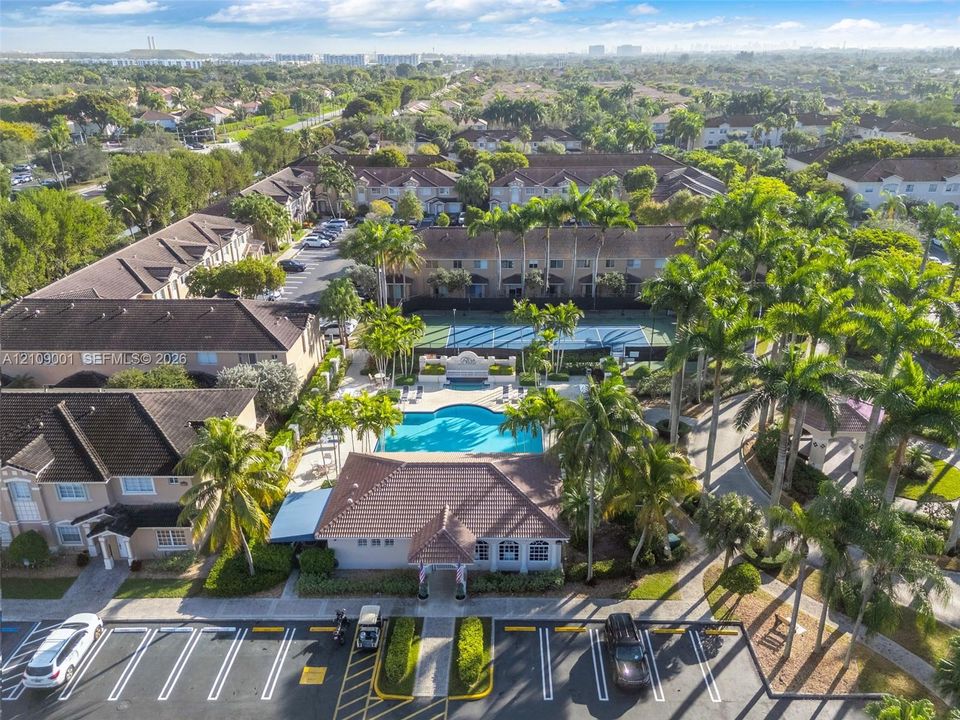 Aerial perspective of residential community featuring a swimming pool, tennis court, clubhouse, and mature palm trees