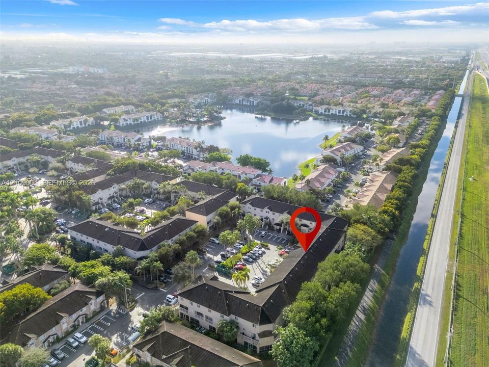 Aerial perspective of a multi-unit residential community featuring dark-tiled roofs, stucco exterior finish, landscaped grounds, and proximity to a large body of water
